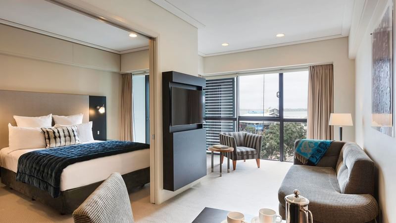 TV lounge with dining area and adjacent bed in Marina View One Bedroom Suite at The Sebel Auckland Viaduct Harbour
