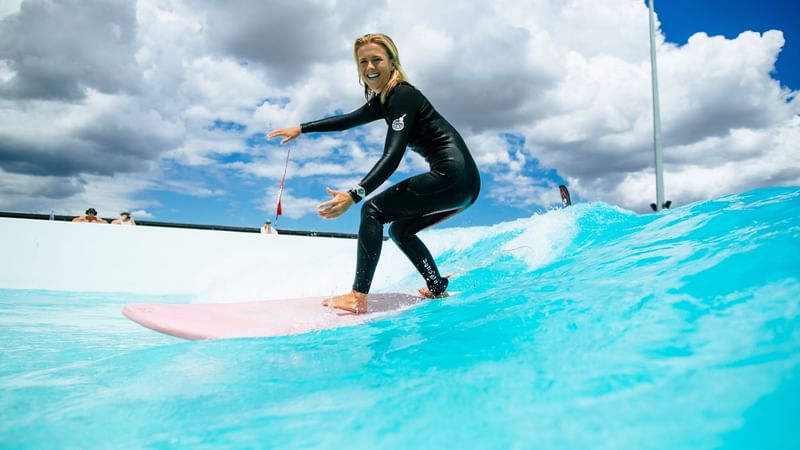 Surfer riding a surfboard on a vibrant blue wave at URBNSURF Sydney near Novotel Sydney Olympic Park