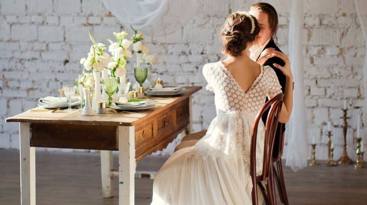 Bride by a groom at a wood table under white drapes near the brick wall at Camino Real Pedregal Mexico