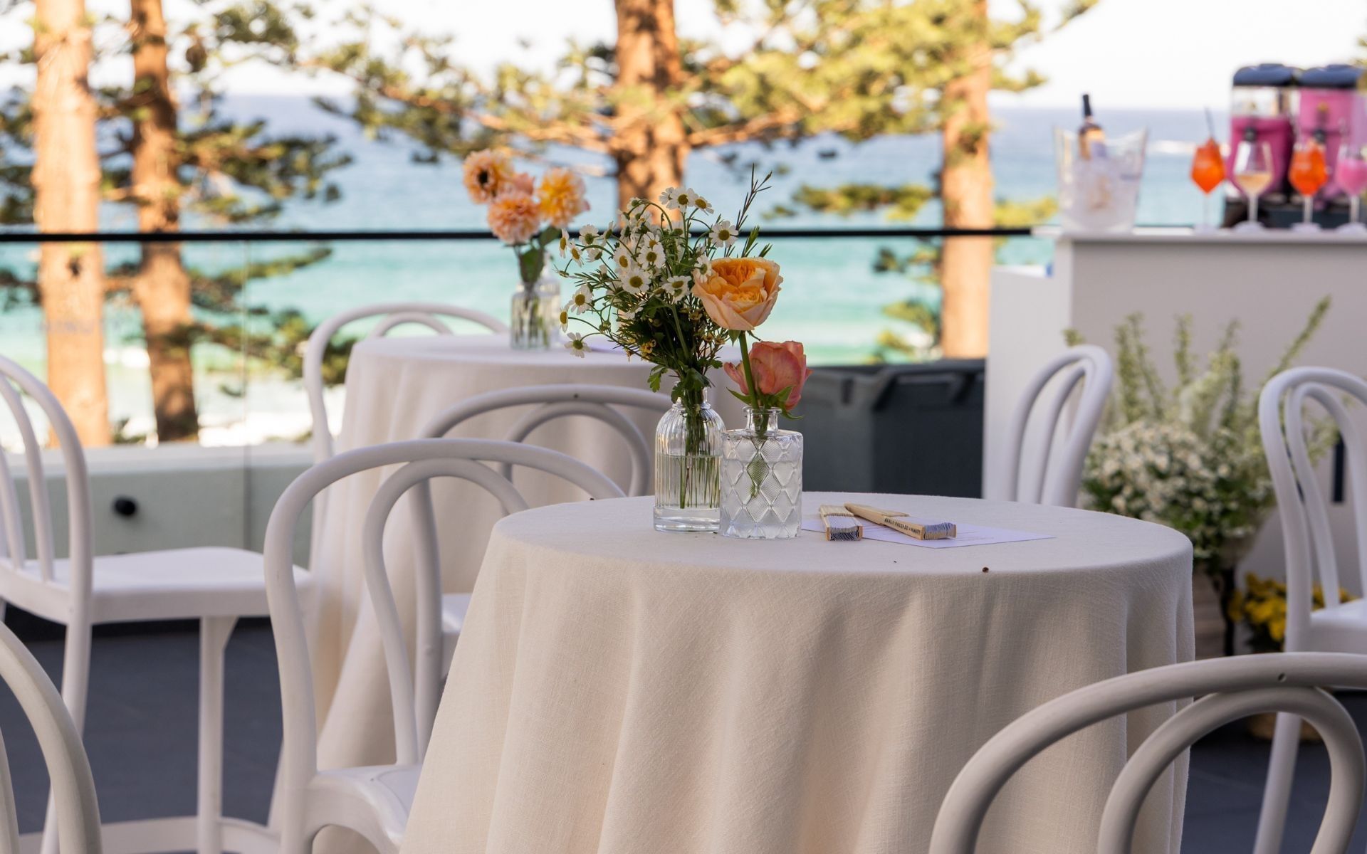 Elysium Manly wedding terrace featuring round tables set with delicate floral vases overlooking pine trees and the sea