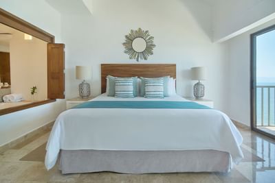 An elegant resort suite bedroom with a king bed looking out to a private oceanfront balcony.
