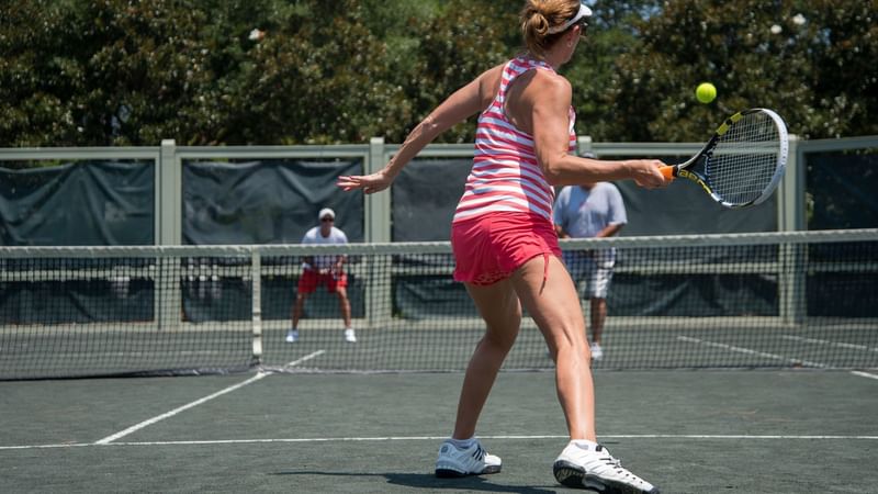 A girl playing tennis on a court near WaterColor Inn