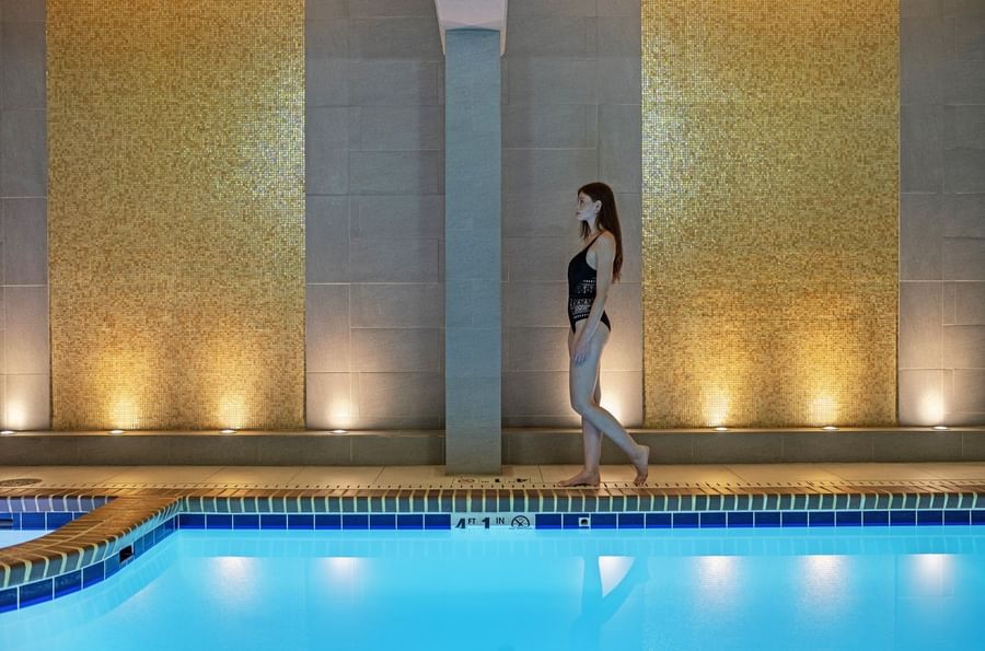 Guest in a swimsuit by an indoor pool under gold mosaic walls at Warwick Seattle