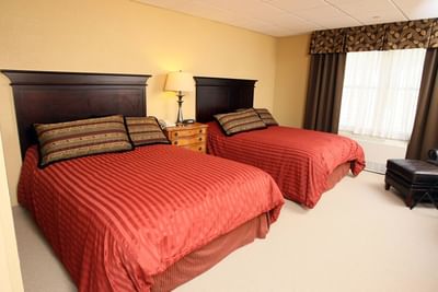 A spacious hotel room featuring two queen-sized beds with striped red comforters at The Pointe at Castle Hill