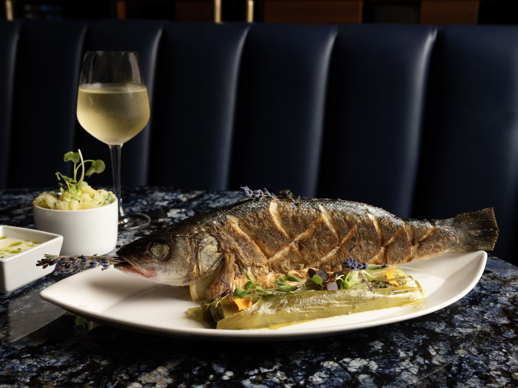 Branzino on a plate with a glass of white wine next to it