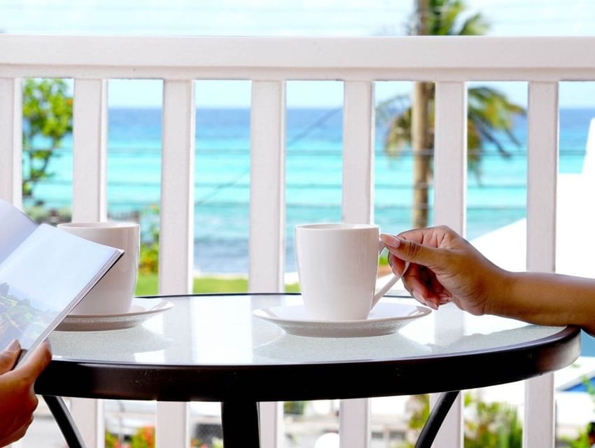 White coffee cups on a glass table beside hands holding a magazine with an ocean view at Worthing Court Apartment