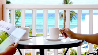 White coffee cups on a glass table beside hands holding a magazine with an ocean view at Worthing Court Apartment