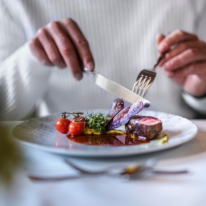 A person cutting steak with tomatoes on a plate at Falkensteiner Hotel Schladming