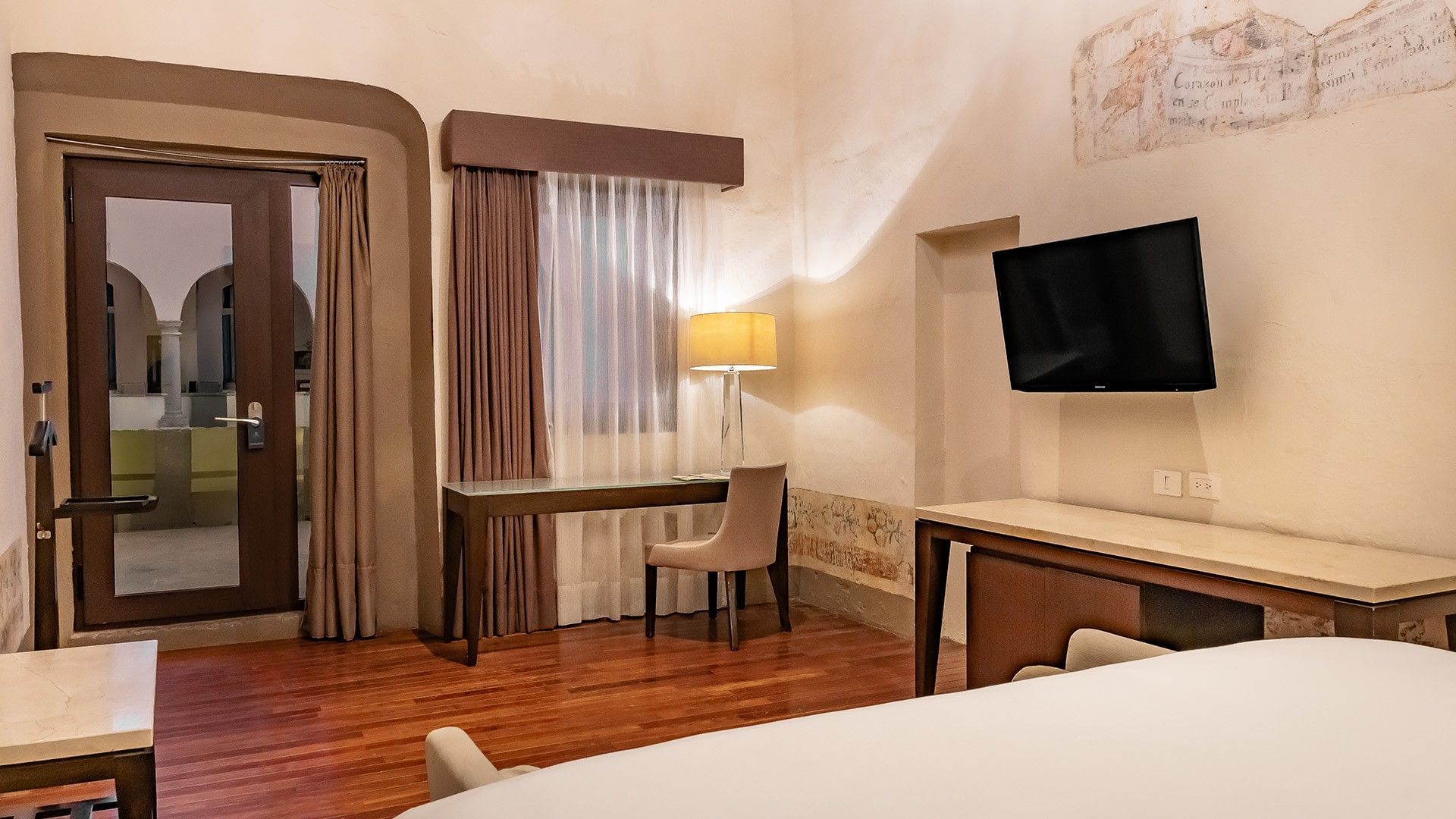 King Novicia interior featuring a glass-top desk, a tan chair, and a wall-mounted TV at Quinta Real Puebla
