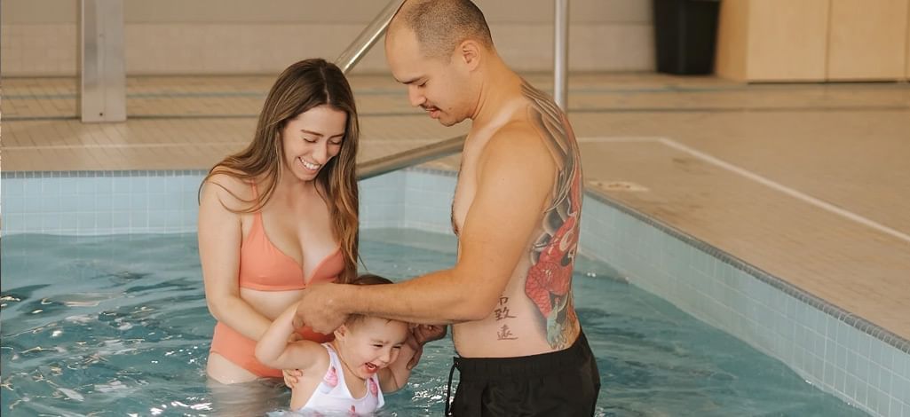 A couple with their young child enjoying a fun moment in a hotel hot tub, showcasing family-friendly amenities.