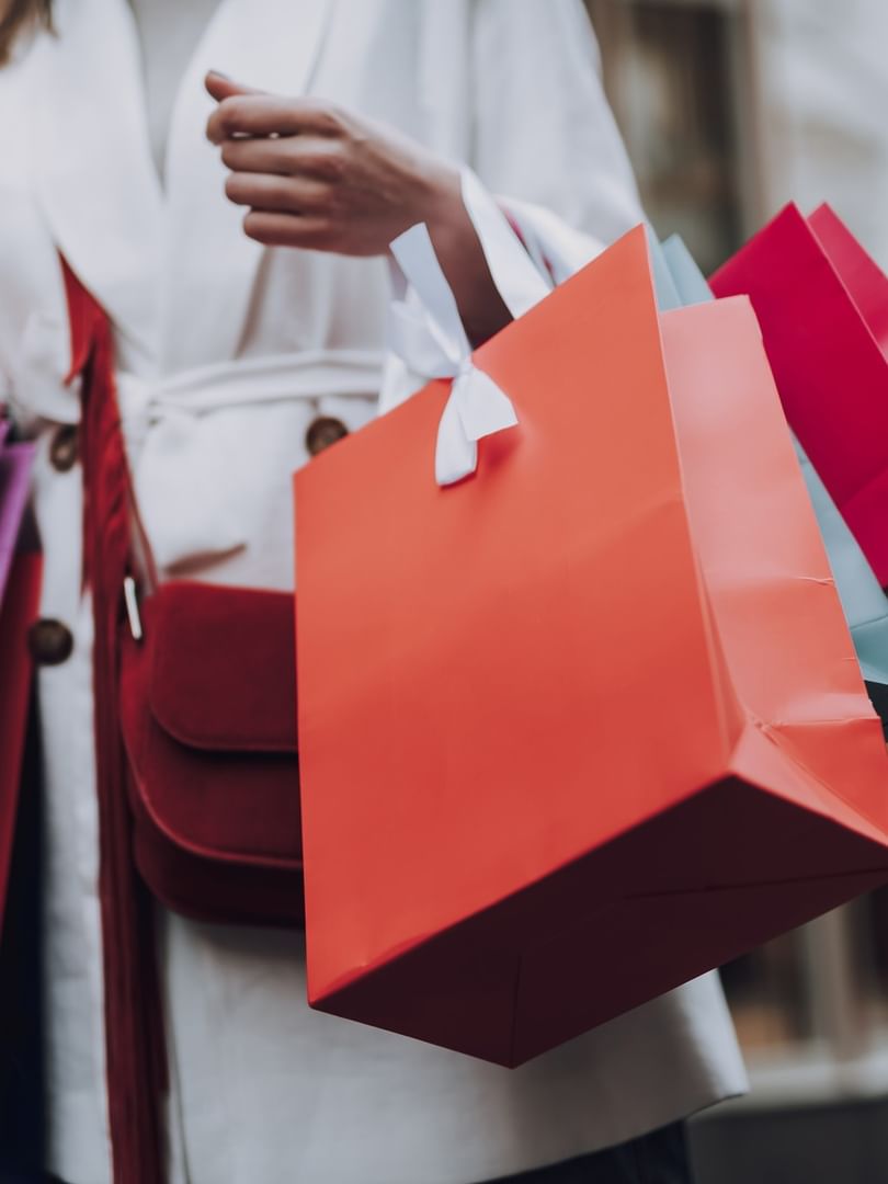 Shopper in a white coat holding colorful gift bags while walking near the storefronts at Warwick Allerton Chicago