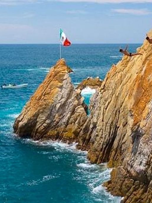 A man jumping off a cliff to the beach at La Quebrada Cliff Diving Show