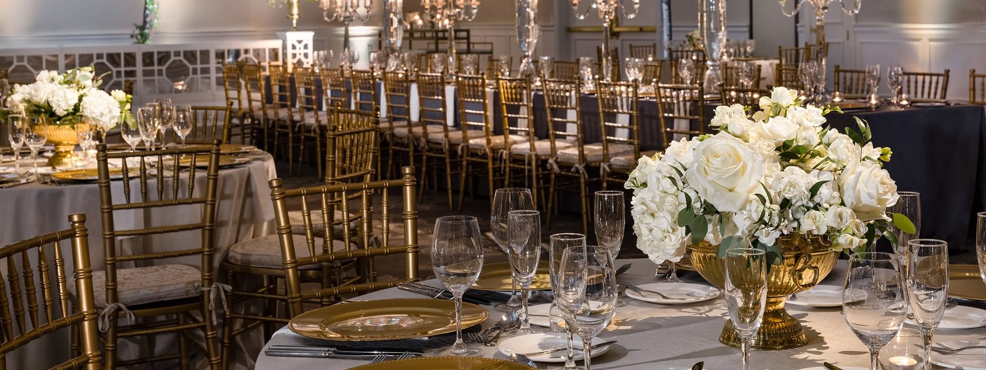 Long dining tables with gold chairs under white floral towers in Turtle Creek Ballroom B at Warwick Melrose Dallas