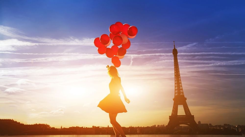 Silhouette of a girl dancing with red balloons under a sunset sky near the Eiffel Tower, Hotel Westminster Paris