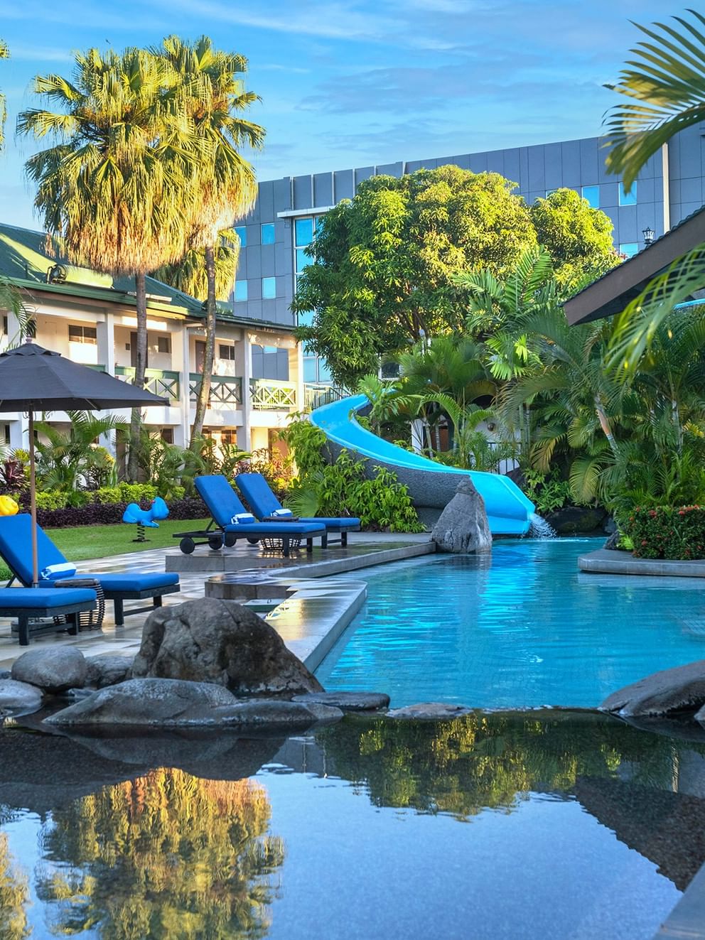 Bright blue loungers under a black patio umbrella by a winding swimming pool at TokaToka Resort Nadi Fiji