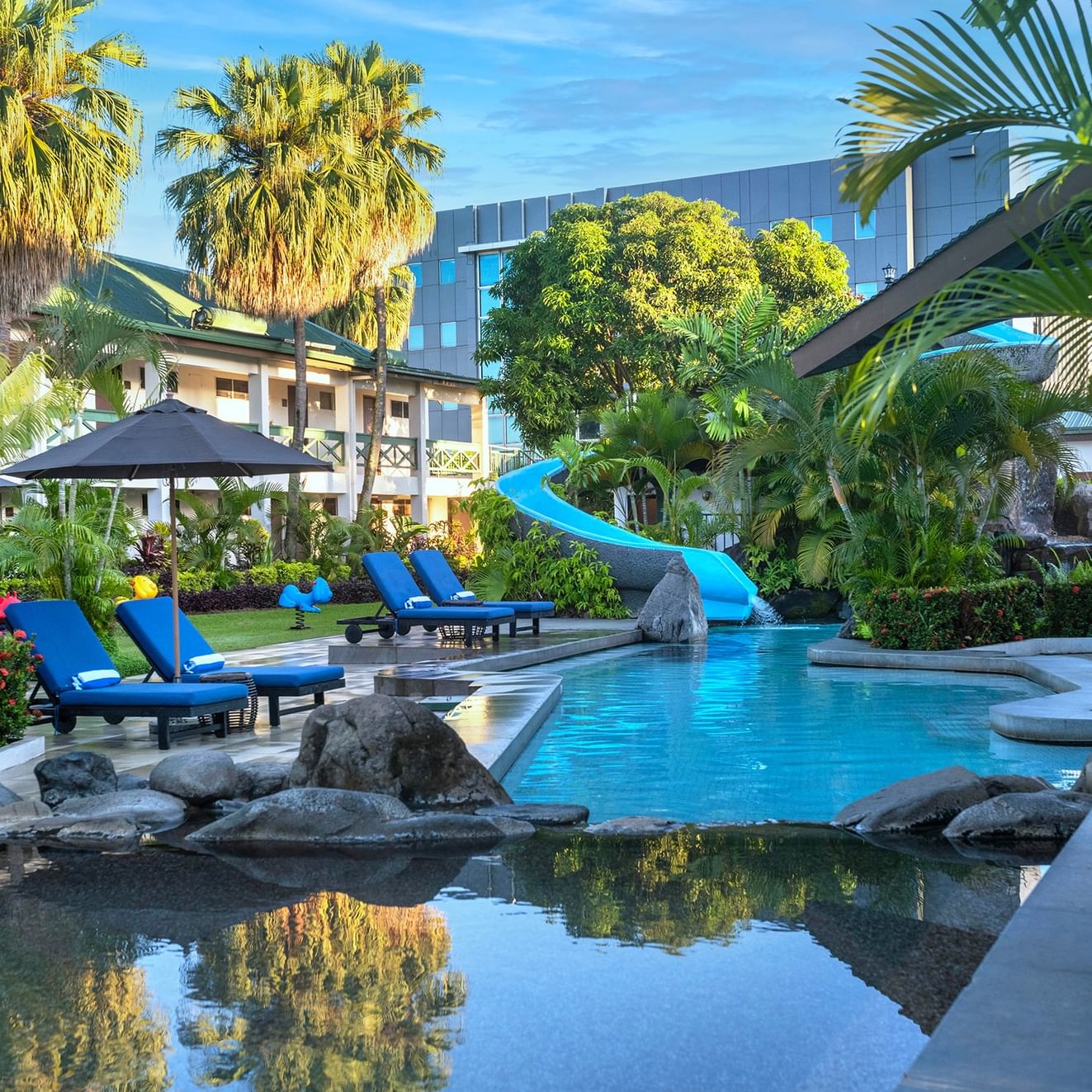 Des chaises longues d'un bleu éclatant sous un parasol noir, au bord d'une piscine sinueuse au TokaToka Resort à Nadi, aux Fidji