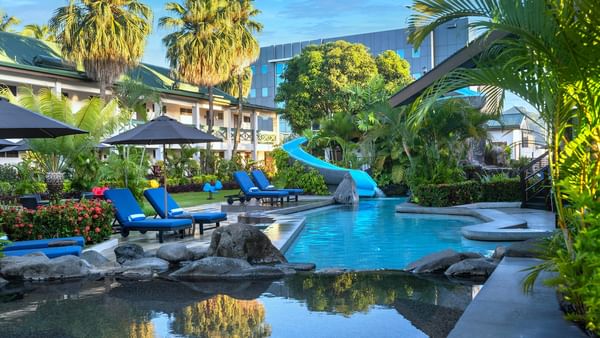Bright blue loungers under a black patio umbrella by a winding swimming pool at TokaToka Resort Nadi Fiji