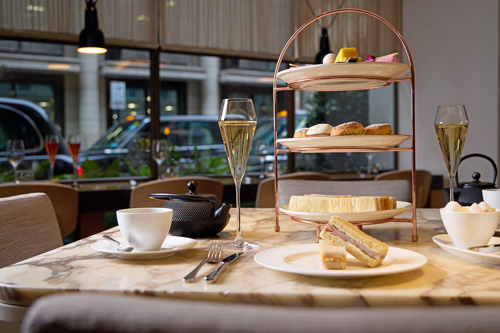 Afternoon tea curated stand with tasty treats, ceramic teapots, cups & champagne served at The May Fair Hotel