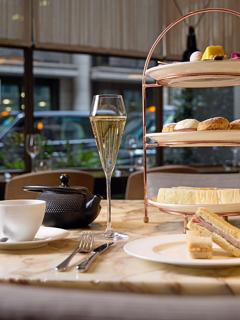Afternoon tea curated stand with tasty treats, ceramic teapots, cups & champagne served at The May Fair Hotel