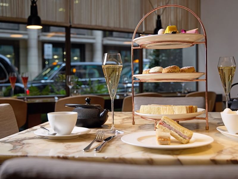 Afternoon tea curated stand with tasty treats, ceramic teapots, cups & champagne served at The May Fair Hotel