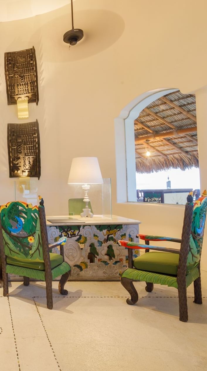 Artistic check-in desk featuring vibrant bird-motif chairs and warm ambient lighting at Quinta Real Acapulco