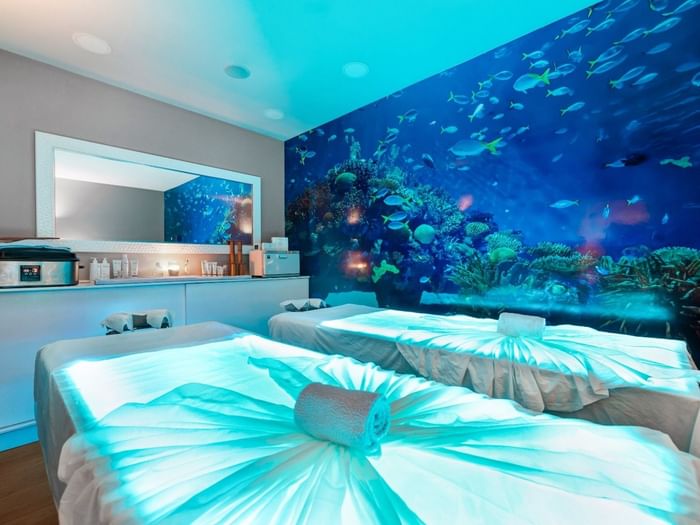 The tranquil couples spa room at Hotel Do Caracol, featuring glowing massage tables and an aquatic mural