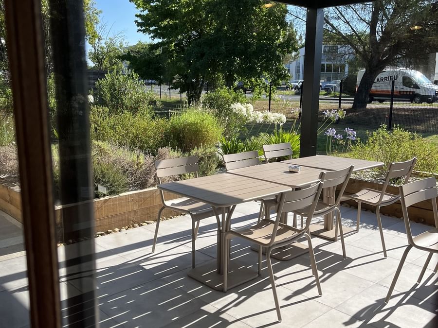 Sunny outdoor terrace featuring modern metal tables and chairs surrounded by lush garden greenery at Hotel Bordeaux Airport