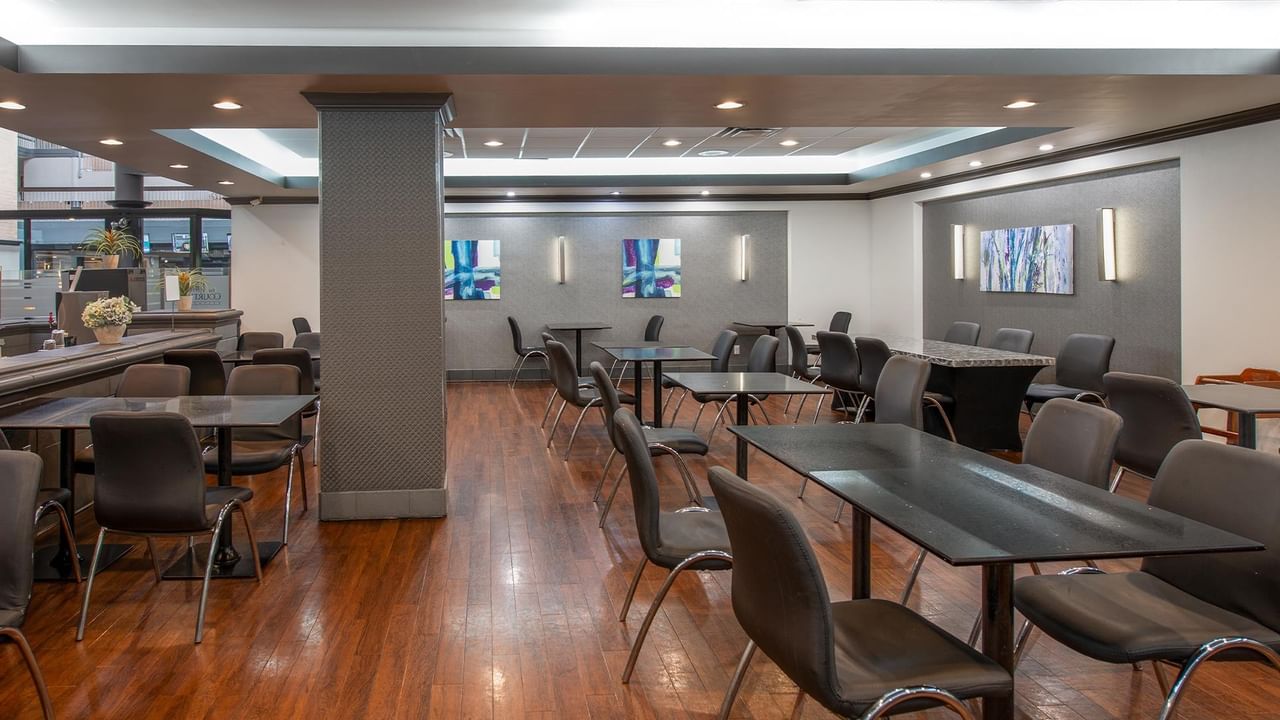 Modern dining area with dark tables, gray chairs, and colorful artwork on walls at Coast Calgary University Area Hotel by APA