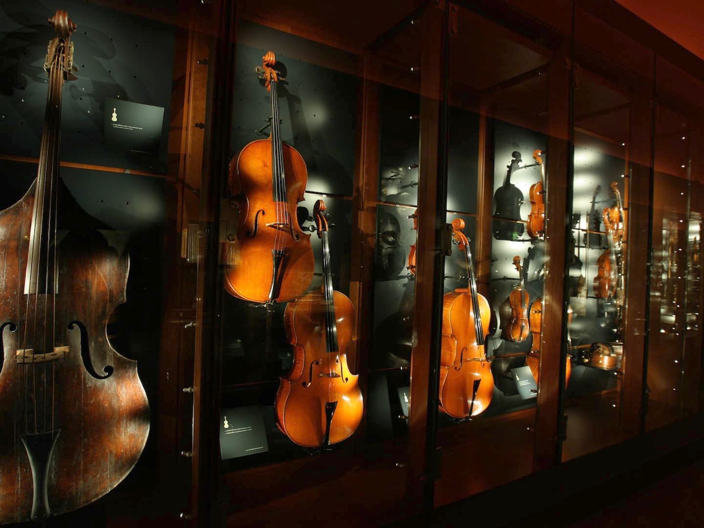 Violins and a cello glow in a glass case at the National Museum of Musical Instruments near The Glam Hotel