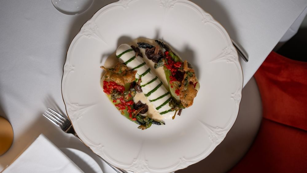 Plated seared fish dish with herbs, placed by a fork & napkin on a table, served in Le Céladon at Hotel Westminster Paris