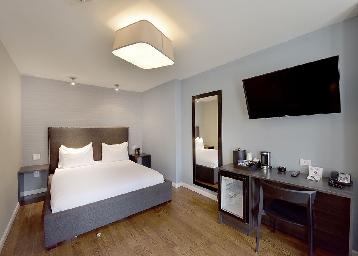 A hotel room with a queen-sized bed, desk, TV, and mirror