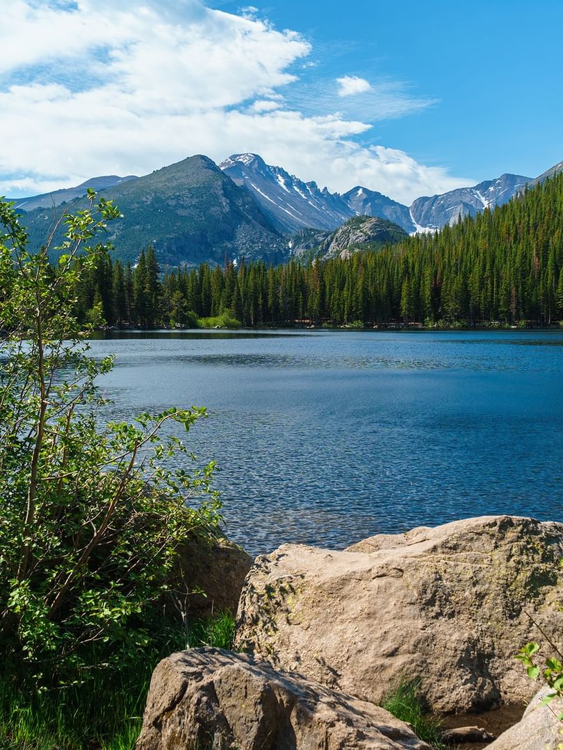 Bear Lake with large rocks under a pine forest with snowy mountain peaks near Warwick Denver