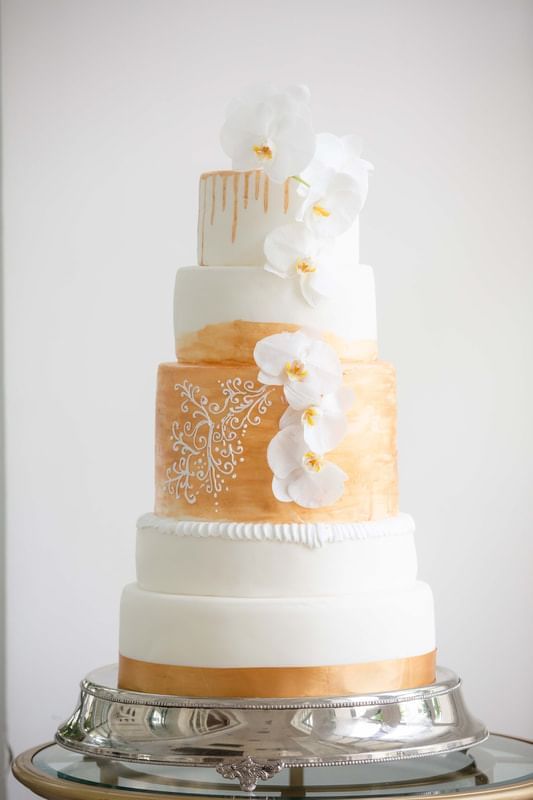 Elegant five-tier wedding cake with white fondant, gold accents, intricate patterns, and white orchid at Park Hyatt Saigon