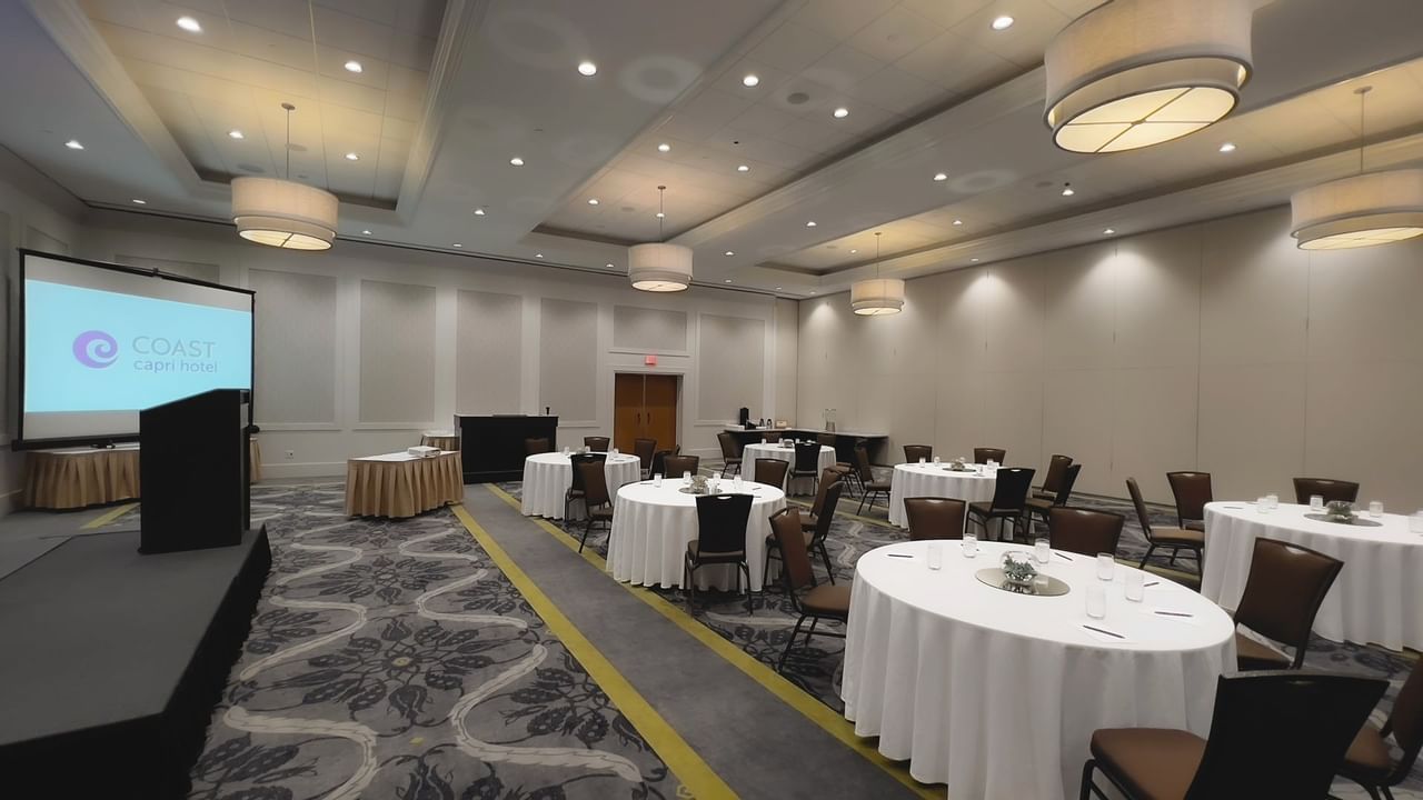 Ballroom with round tables, chairs, stage, podium and presentation screen