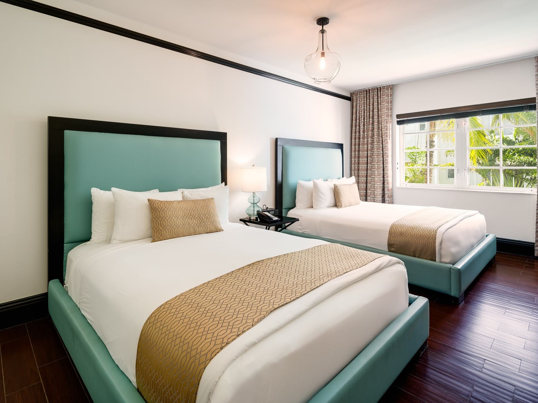 Two beds with teal headboards, white bedding, and a window with curtains in a bedroom.