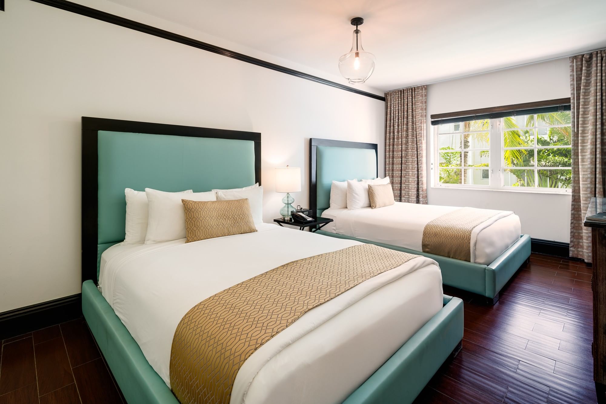 A hotel room with two twin beds, a window, and dark hardwood floors