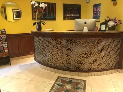 Chelsea Pines Inn reception desk with an Apple desktop, two vases with flowers, and three framed wall decorations