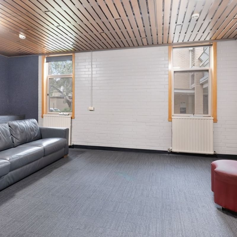 Lounge area with gray leather couch and red ottoman at La Trobe University - Glenn College.