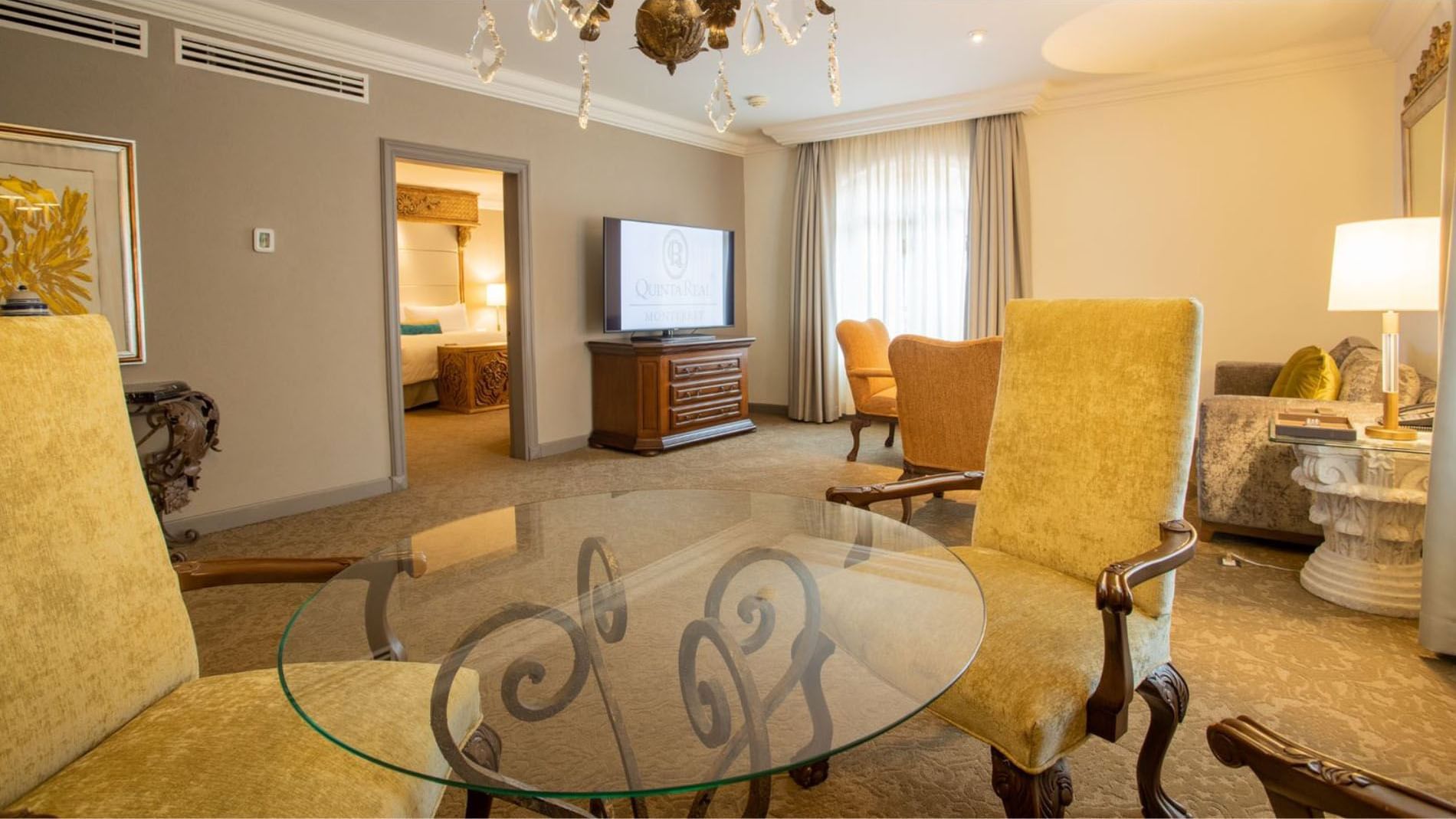 King Governor Suite living area featuring yellow armchairs, a glass table, and a crystal chandelier at Quinta Real Monterrey