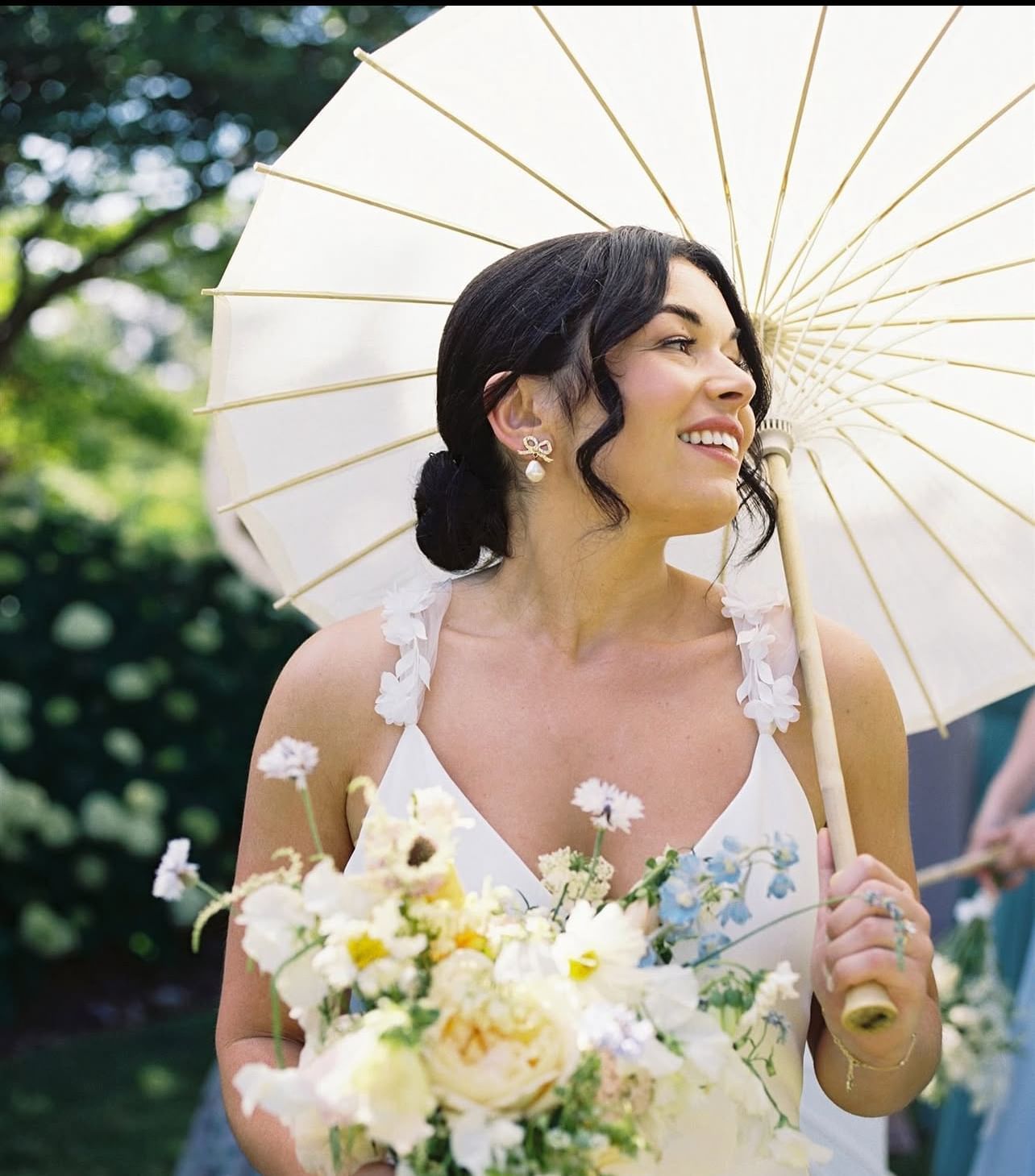 Smiling bride holding white parasol and floral bouquet, standing outdoors at The Clifton Hotel in Charlottesville, VA.