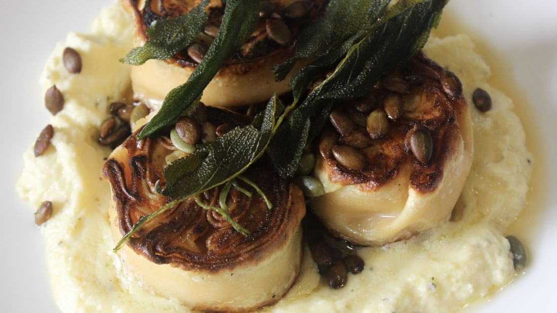 Plate with three scallops in creamy sauce garnished with herbs and seeds, highlighting Karinya’s Refreshed Menu.