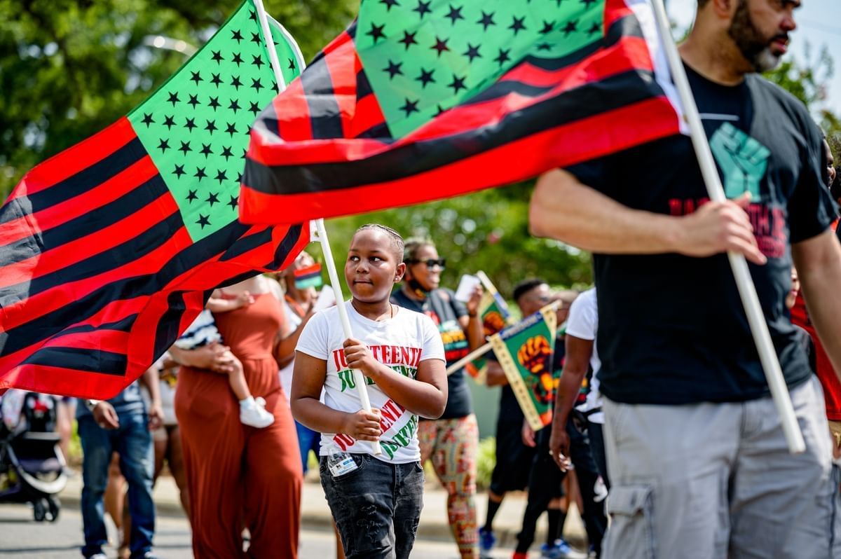 People marching in a Juneteenth walk carrying red, black, and green flags.