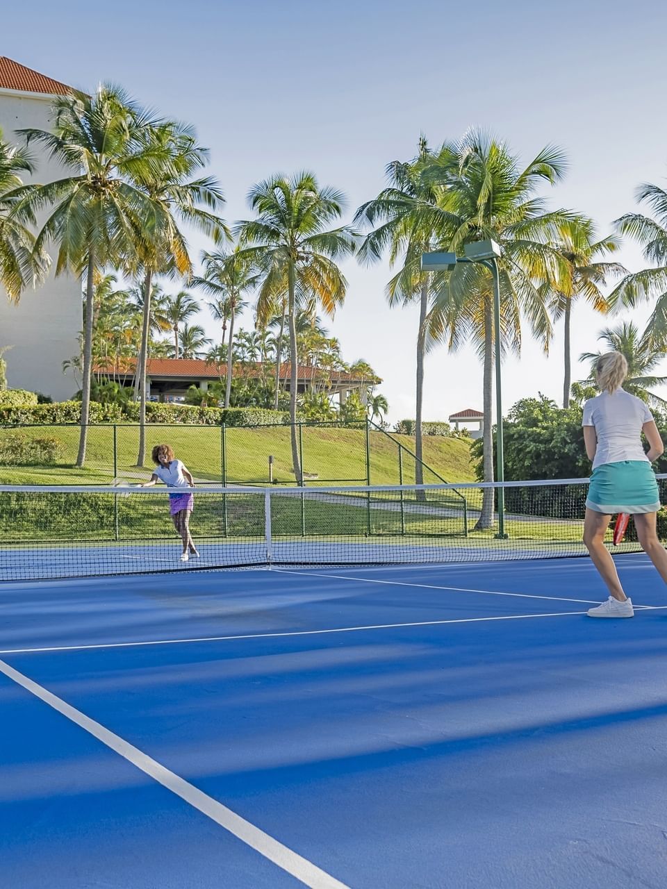 2 personas jugando tenis en la cancha azul frente al resort El Conquistador Resort