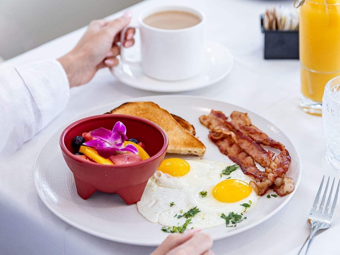 Person enjoying breakfast with eggs, bacon, toast & fruit bowl at The Savoy Hotel & Beach Club