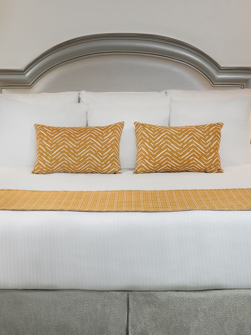 Queen bed with yellow accent pillows by two lamps in Deluxe King at Warwick Melrose Dallas