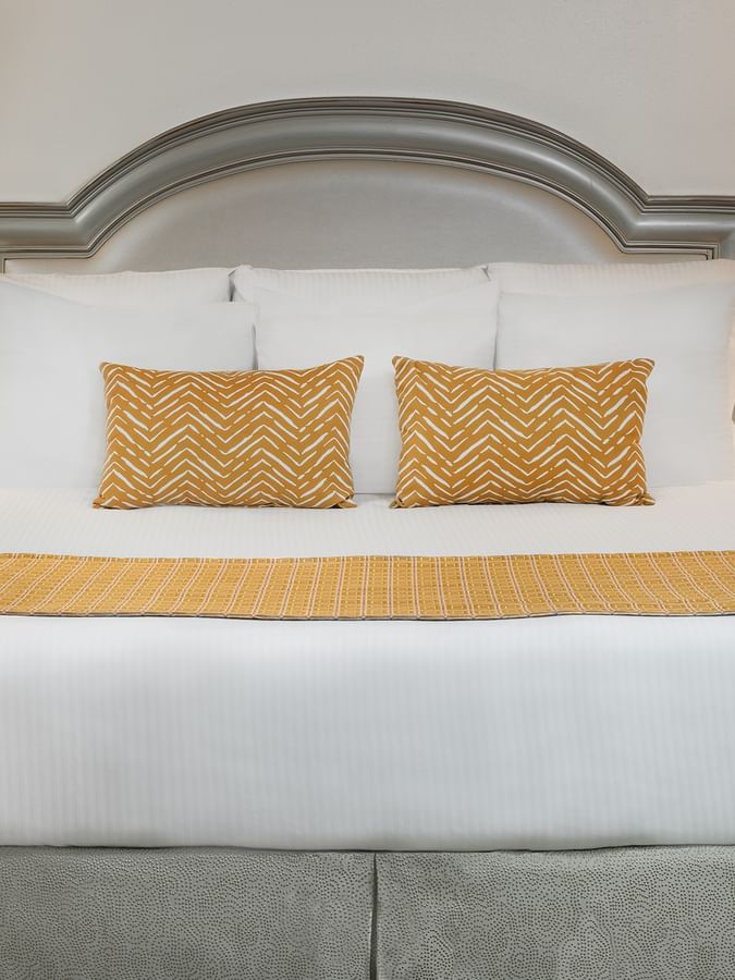 Queen bed with yellow accent pillows by two lamps in Deluxe King  Accessible at Warwick Melrose Dallas