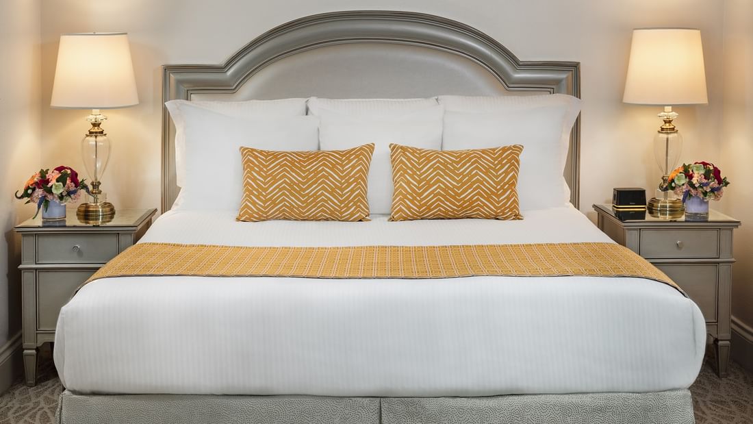 Queen bed with yellow accent pillows by two lamps in Deluxe King at Warwick Melrose Dallas