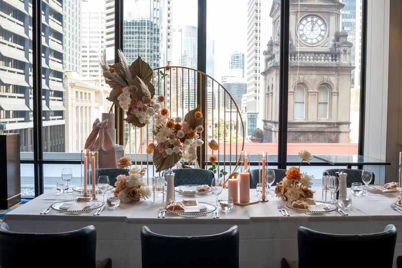 Elegant dining table with floral centerpiece against a cityscape backdrop at Sofitel Brisbane Central