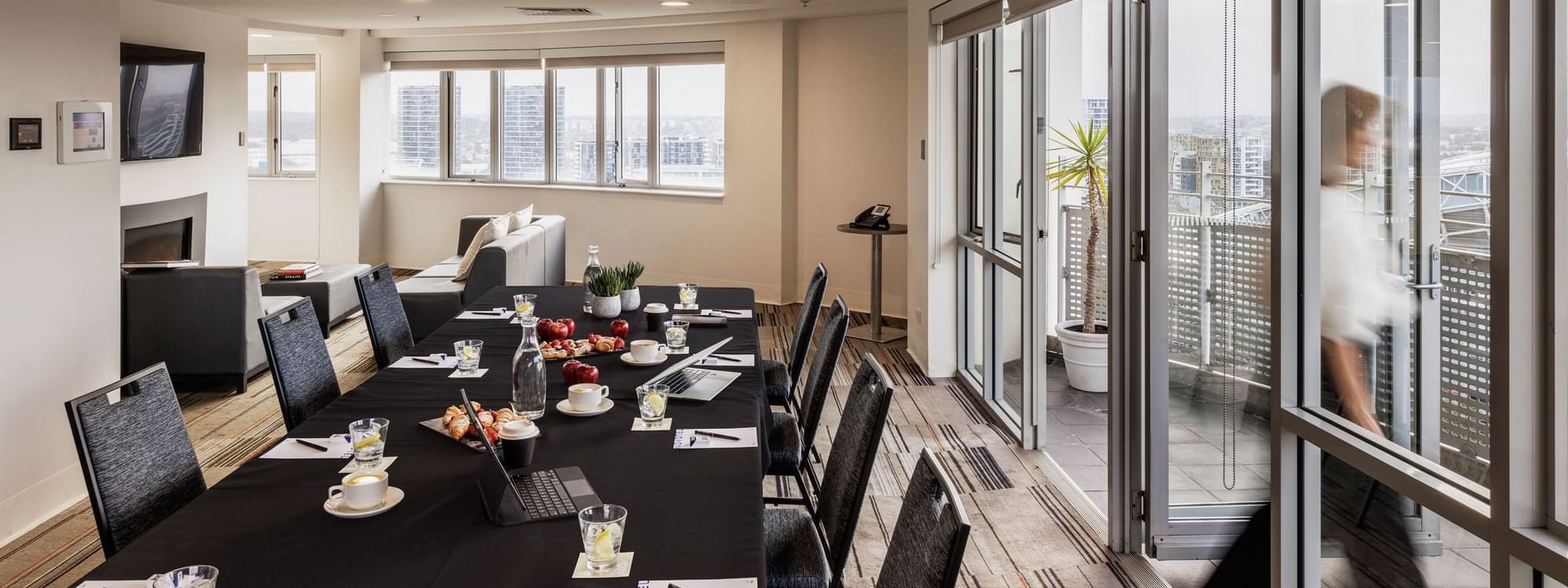The Lounge with table set-up, refreshments, and a city view through large windows at Novotel Sydney Olympic Park