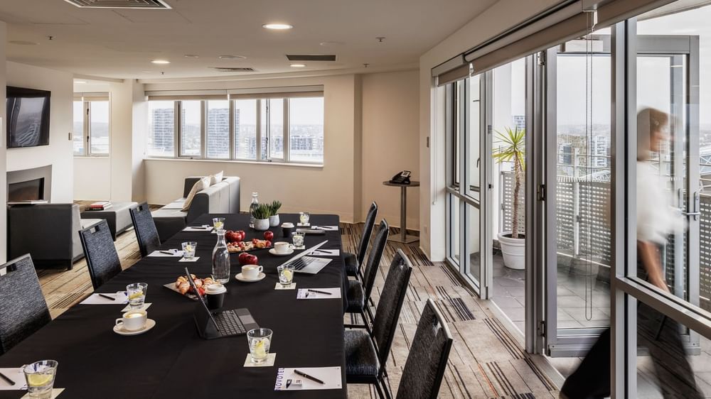 The Lounge with table set-up, refreshments, and a city view through large windows at Novotel Sydney Olympic Park